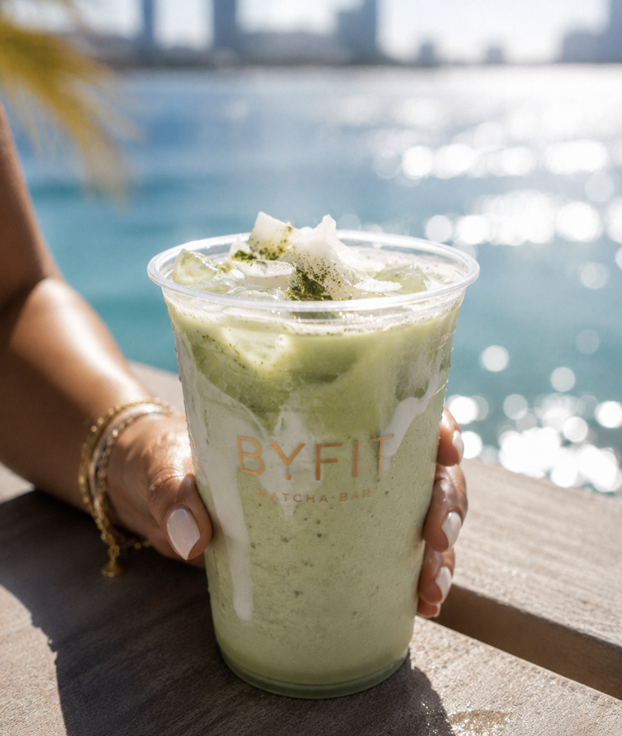 Matcha BYfit servido en la playa junto a un batidor de bambú al atardecer